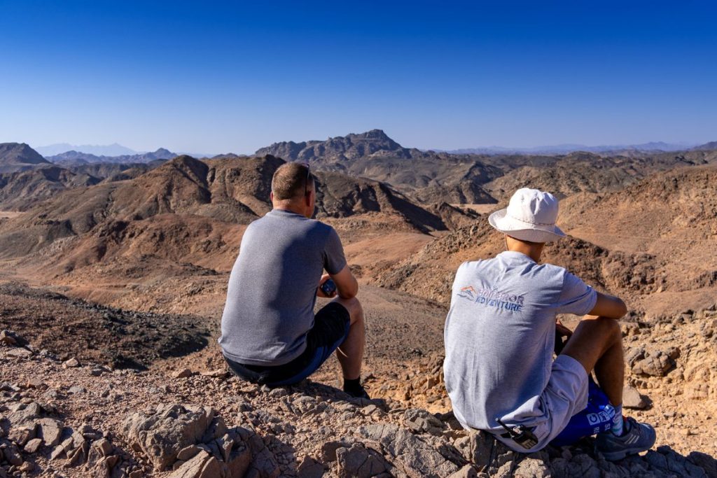 Hikers sit on top of an Egyptian mountain looking across the desert